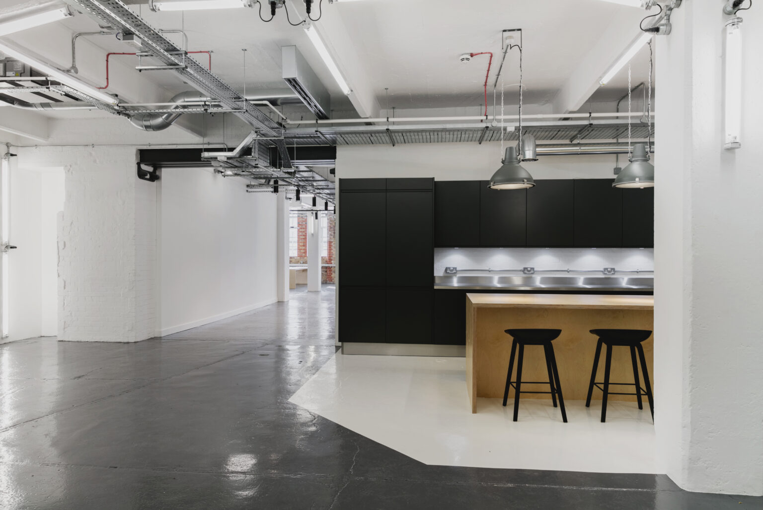 Workspace kitchen at the Tea Building: matt black cabinetry, stainless steel worktop and plywood island with black stools